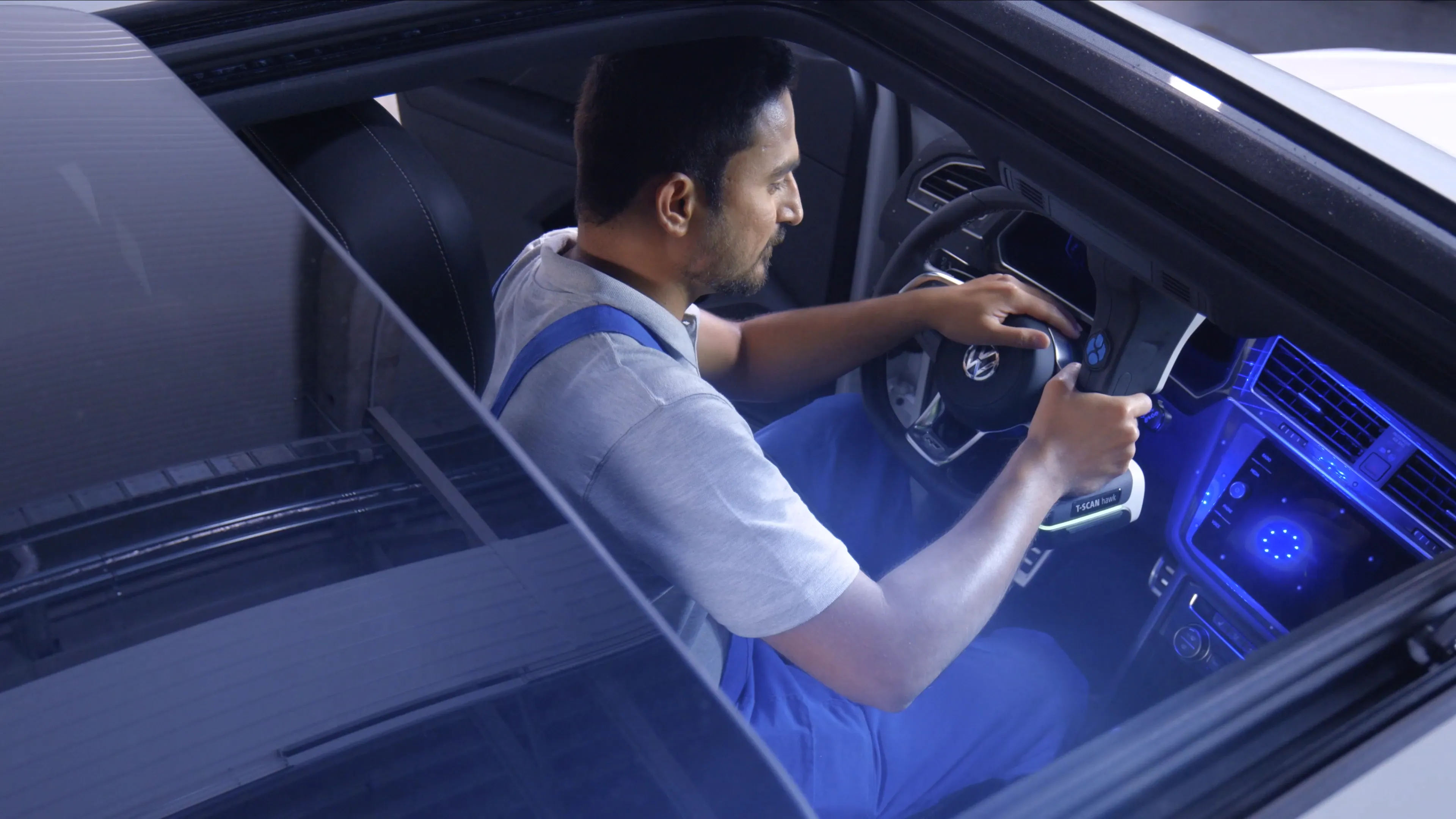 Ein Techniker sitzt in einem Auto und scannt mit einem Handscanner das Amaturenbrett für eine Autoproduktion.