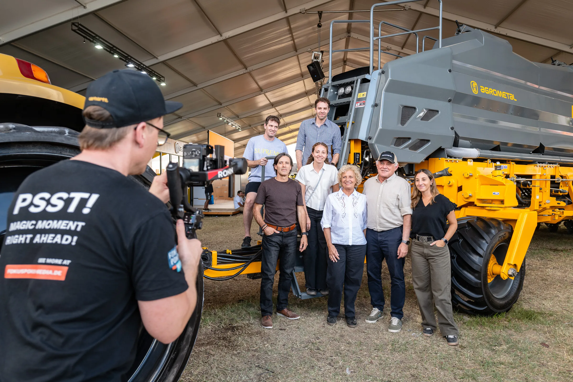 Ein Kameramann von Fokuspokus im Vordergrund fotografiert ein Gruppenbild vor einer Erntemaschine.