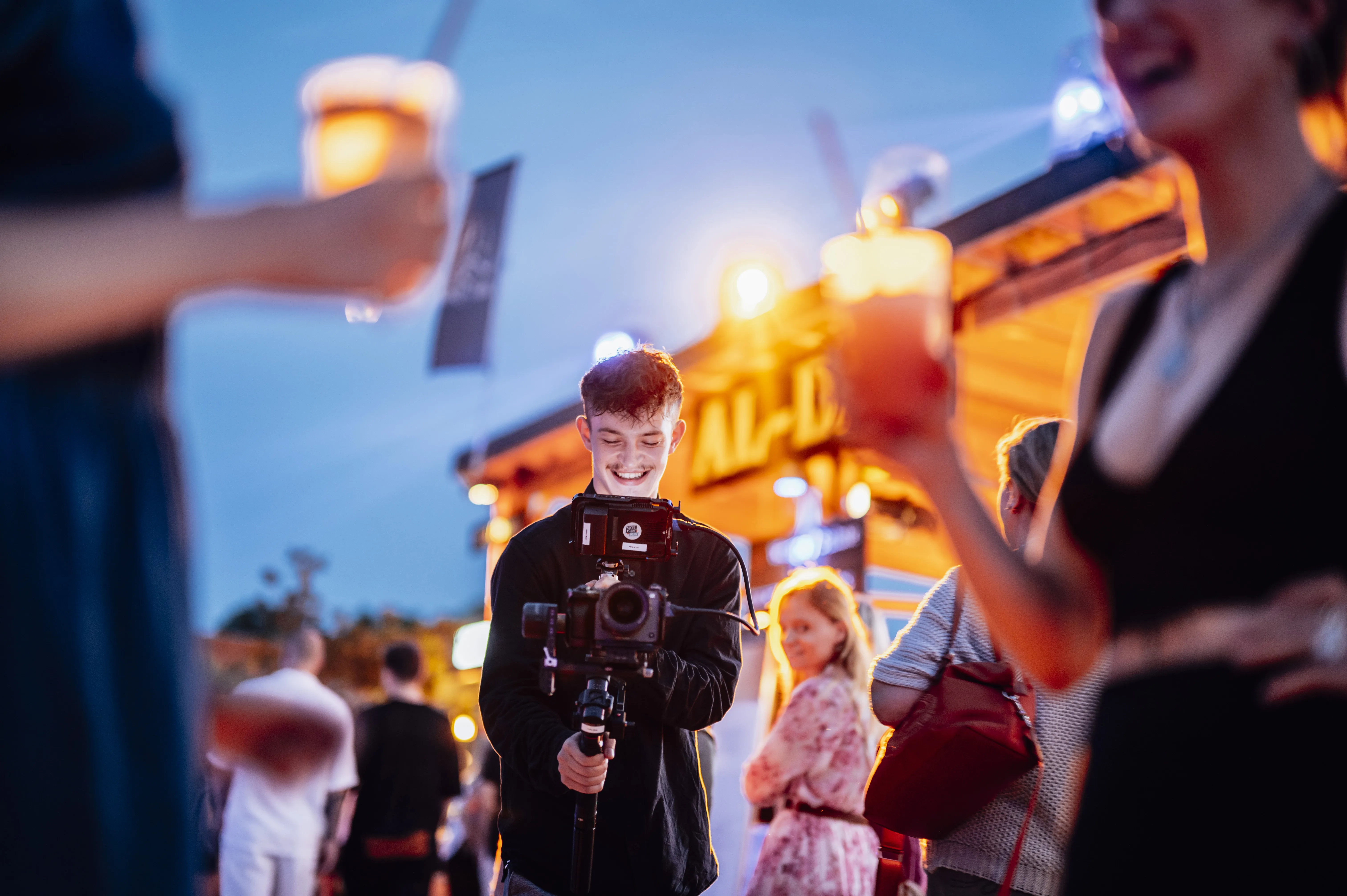 Ein Kameramann filmt zwei Frauen mit Gläsern in der Hand auf dem Maschseefest in Hannover für einen Eventfilm