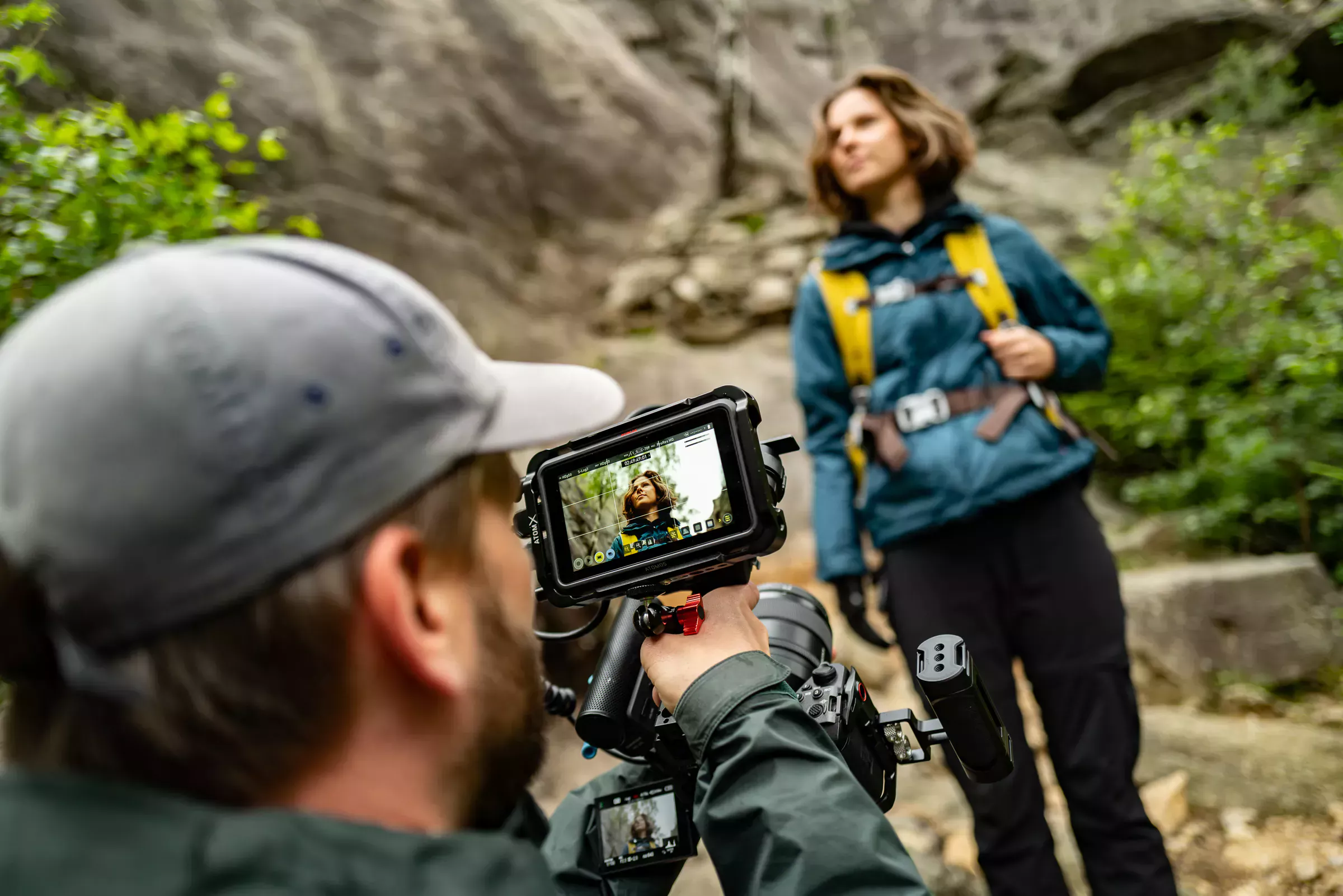 Beim Dreh einer Werbekampagne in der Natur filmt ein Kameramann die Protagonistin mit blauer Jacke vor einem Felsen.