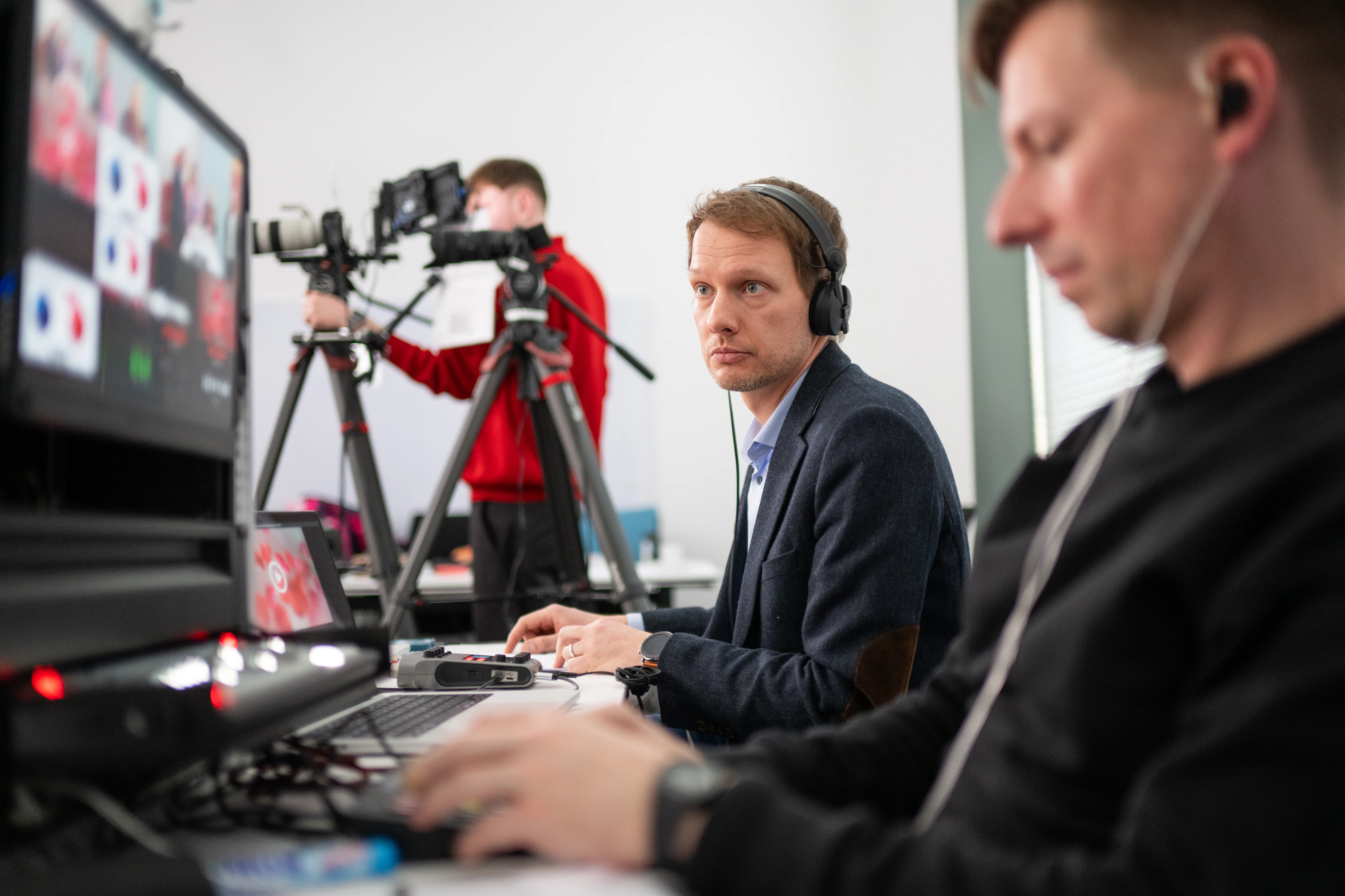 Ein Projektmanager für einen Livestream in Hannover schaut auf einen Monitor bei einer Live-Übertragung für die Sparkasse. Im Hintergrund steht ein Kameramann an einer Kamera, im Vordergrund bedient ein Regisseur die Technik.