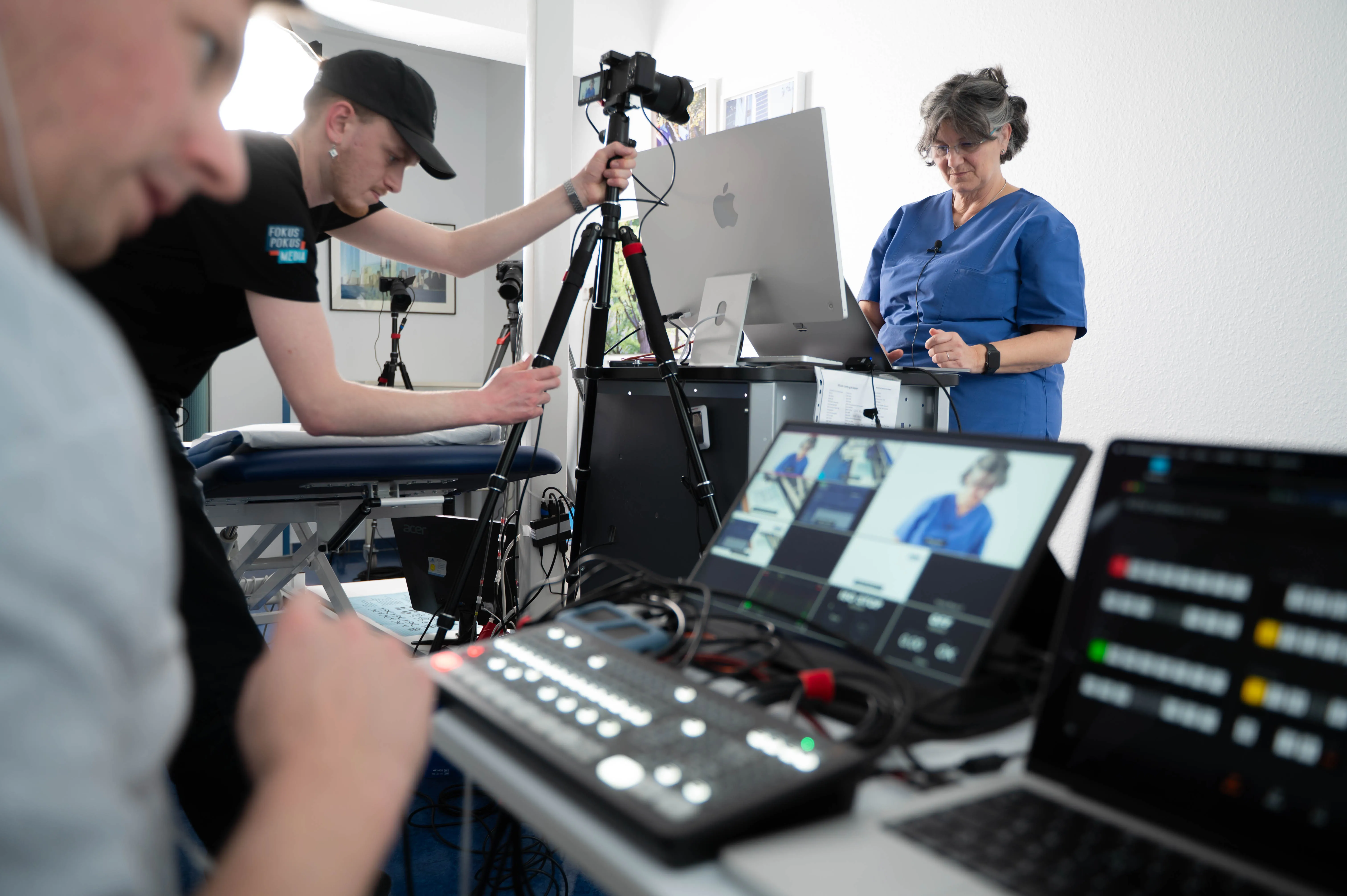 Ein Livestreaming-Team aus zwei Personen bedient die Technik. Im hintergrund ist eine Protagonistin zu erkennen.