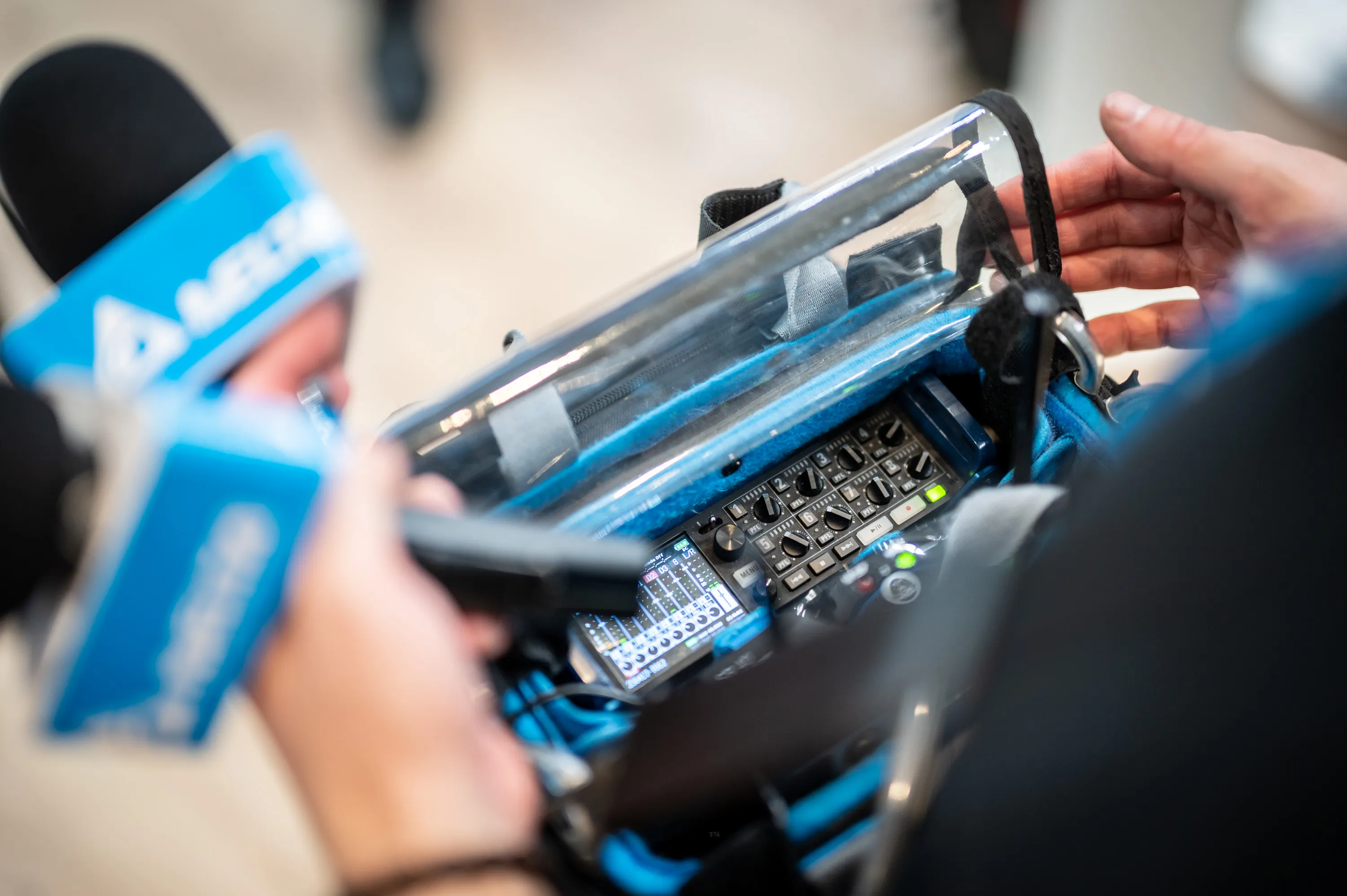 Eine Hand, die zwei Mikrofone mit dem Logo von Delta Elektroniks hält und ein Tonaufnahmegeraet bedient.