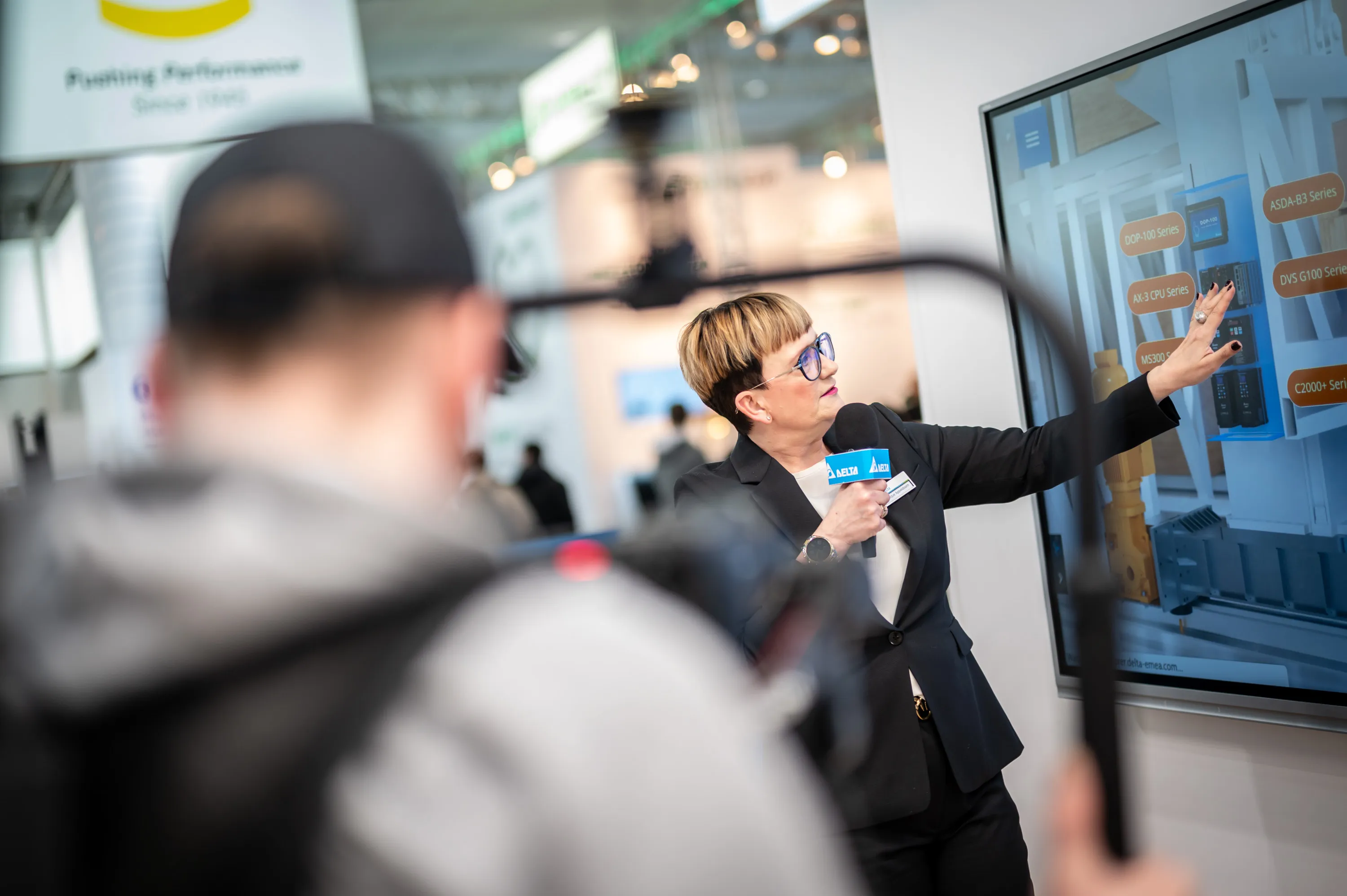 Moderatiorin zeigt auf einen Monitor am Messestand von Delta in Hannover