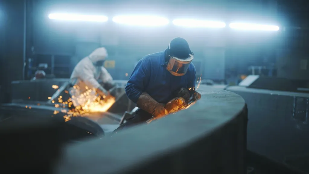 In einer Industriefirma schweißen Männer mit Schutzanzügen ein großes Metallteil für eine Filmproduktion in Braunschweig