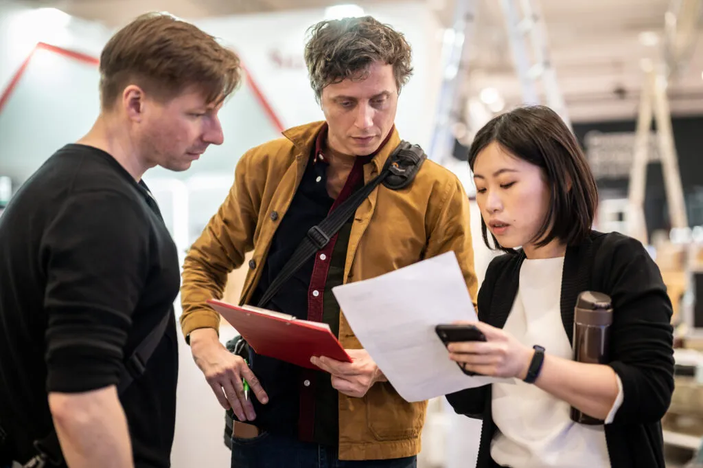 Regisseur, Kameramann und Kunde besprechen den Ablauf einer Filmproduktion auf einer Messe