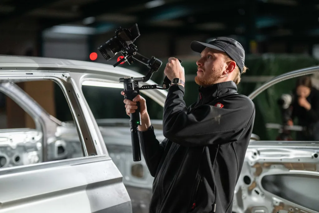 Kameramann mit einem Gimbal beim Filmdreh an einer Fahrzeugkarosse