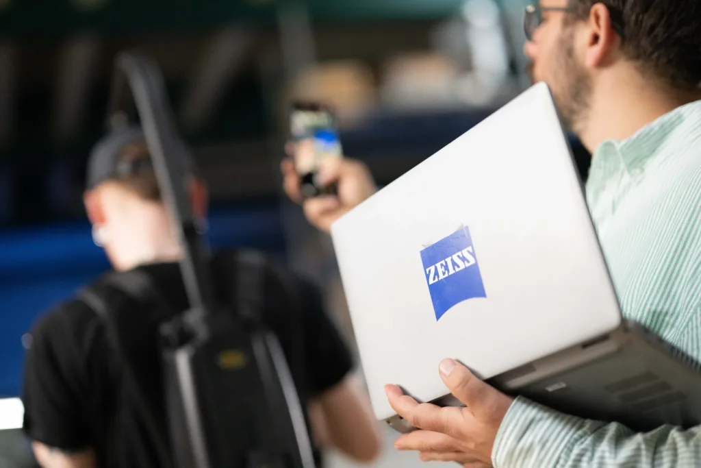 Kunde hält Notebook mit Zeiss-Aufkleber und ein Smartphone in der Hand