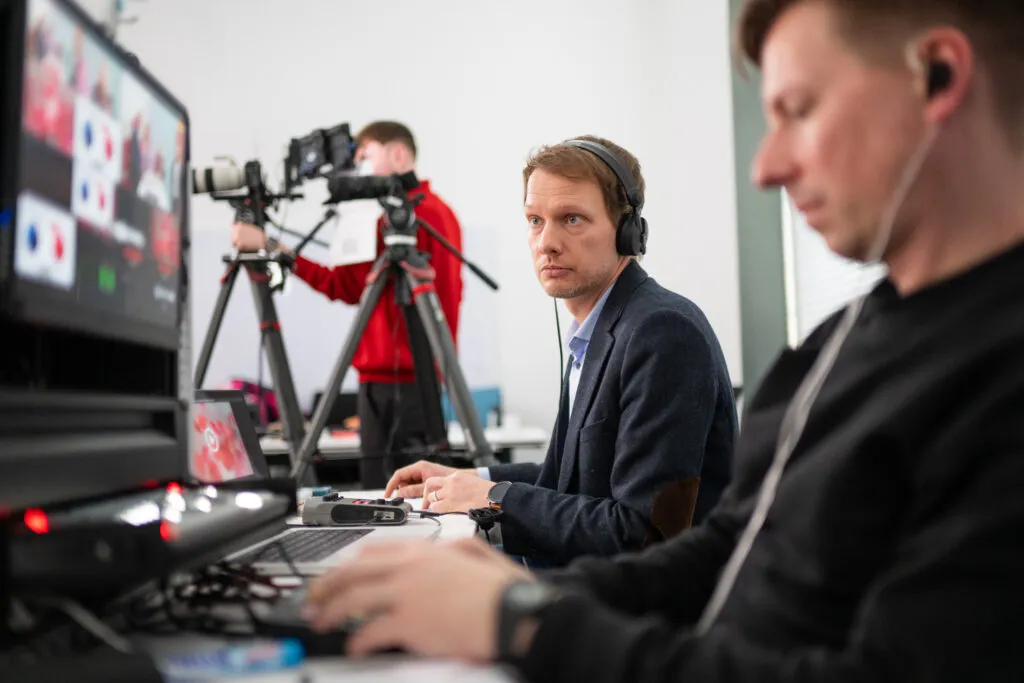 Ein Projektmanager für einen Livestream in Hannover schaut auf einen Monitor bei einer Live-Übertragung für die Sparkasse. Im Hintergrund steht ein Kameramann an einer Kamera, im Vordergrund bedient ein Regisseur die Technik.