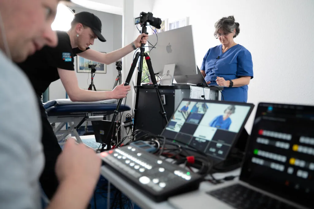 Ein Livestreaming-Team aus zwei Personen bedient die Technik. Im hintergrund ist eine Protagonistin zu erkennen.