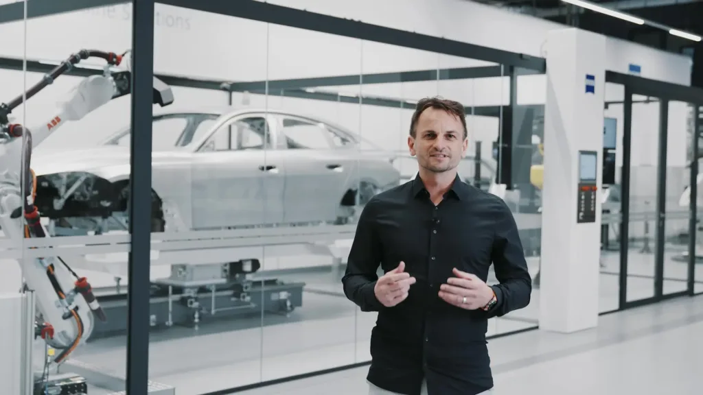 Ein Mann mit schwarzem Hemd steht in einem Showroom vor einer Autokarosserie