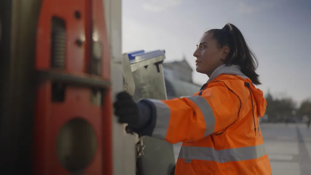 Eine Müllwerkerin lächelt bei der Fahrt auf einem Müllfahrzeug für einen Imagefilm
