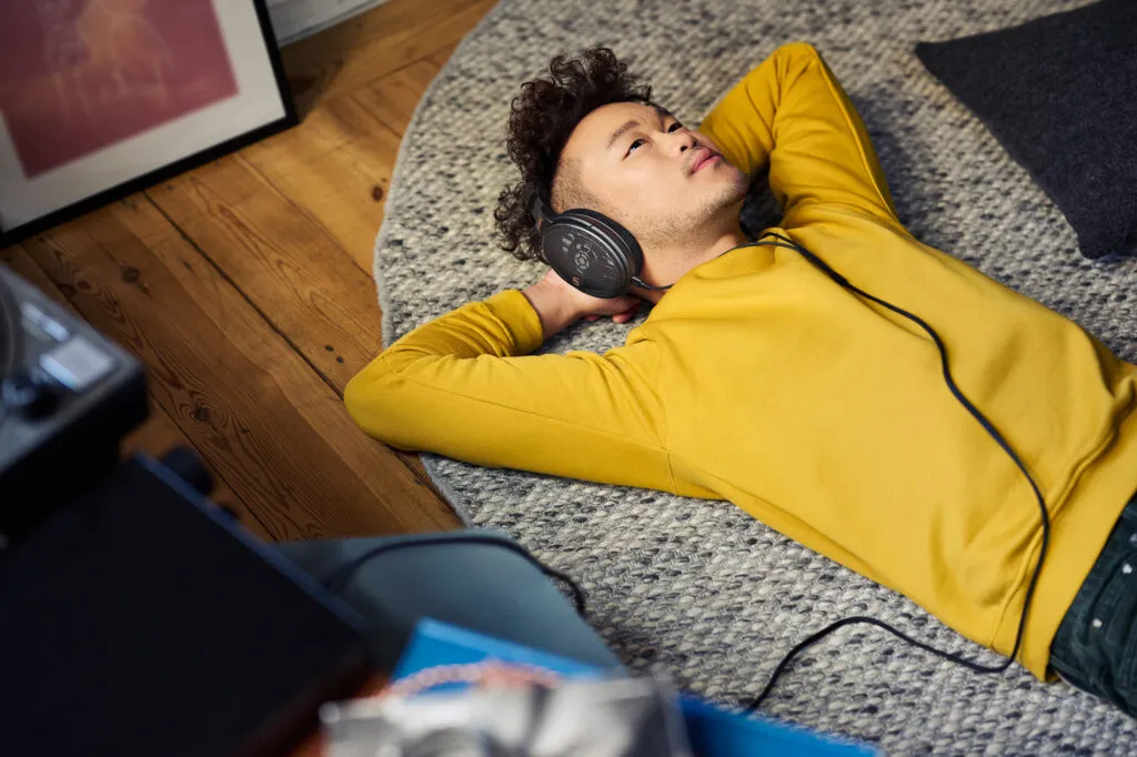 Mann liegt entspannt mit Sennheiser HD 660S2 Kopfhörer auf einem Teppich