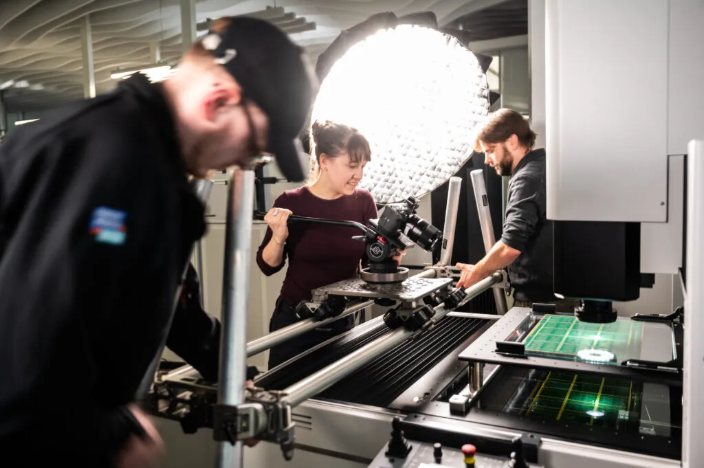 Ein Filmteam macht Videoaufnahmen einer Maschine bei einem Konzern. Im Hintergrund steht eine Licht zur Ausleuchtung.