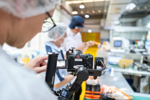 Kameramann filmt in einer Fabrik Arbeiter für eine Filmproduktion in Thailand.