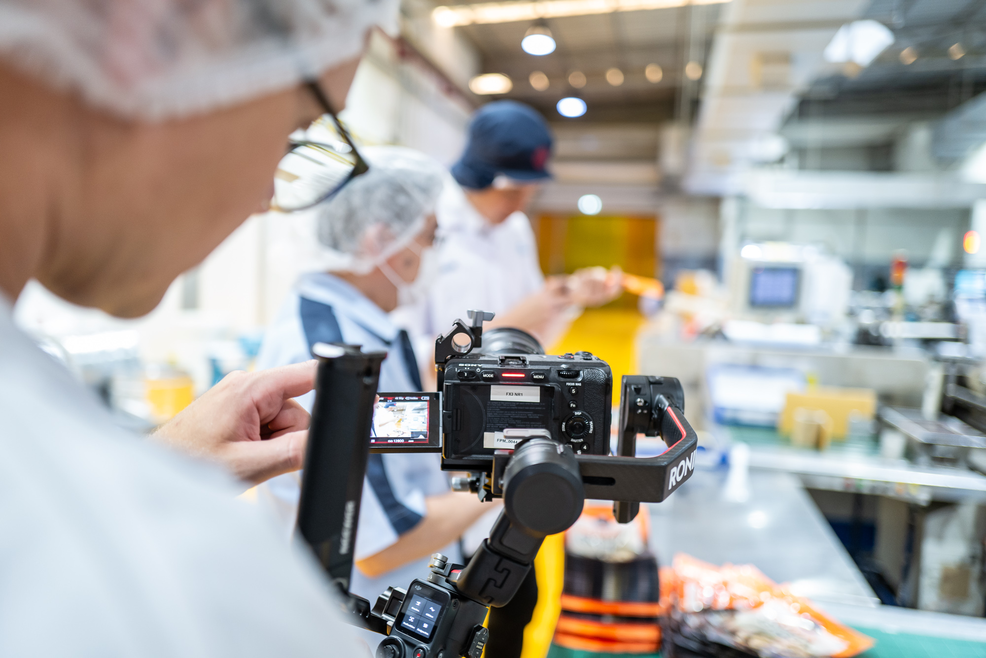 Kameramann filmt in einer Fabrik Arbeiter für eine Filmproduktion in Thailand.