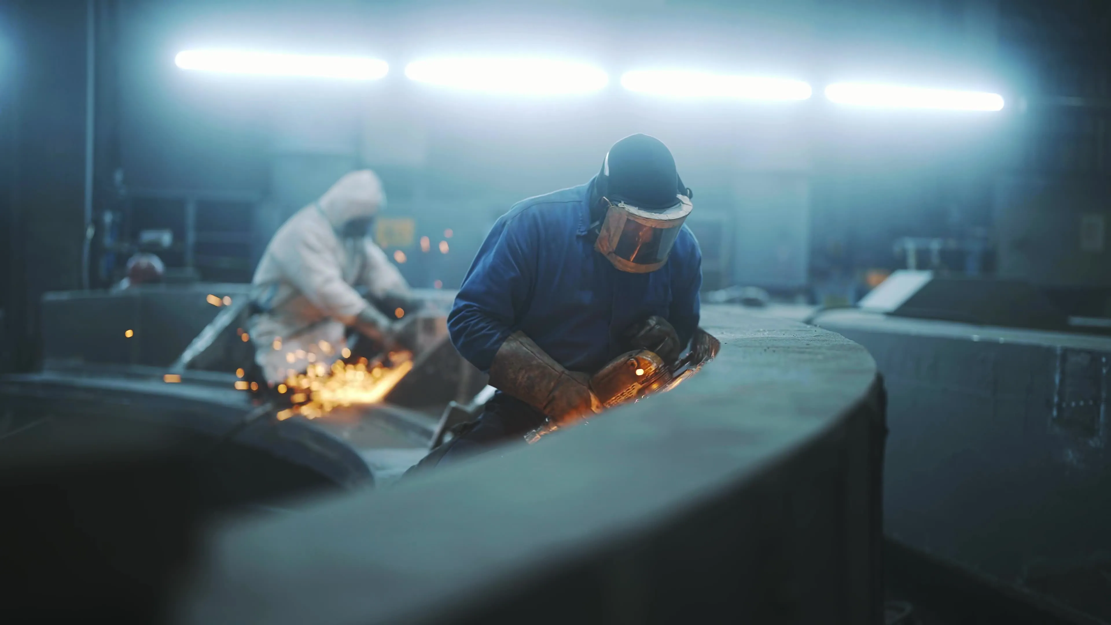 Zwei Stahlarbeiter der firma Siempelkamp schleifen ein Metallstück in einer Fabrik.